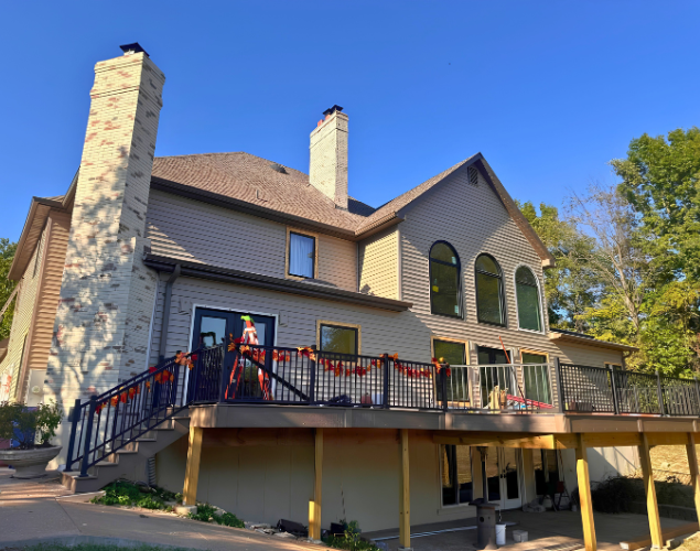 House with stone chimney, raised deck, and red railing in a sunny wooded setting