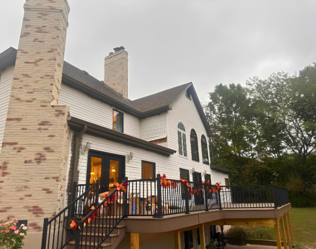 Outdoor deck on a white house decorated with orange pumpkins and black railings at dusk