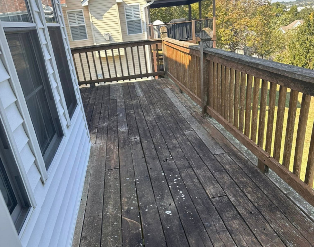 Weathered wooden deck beside a house, with railings and neighboring homes visible in daylight.