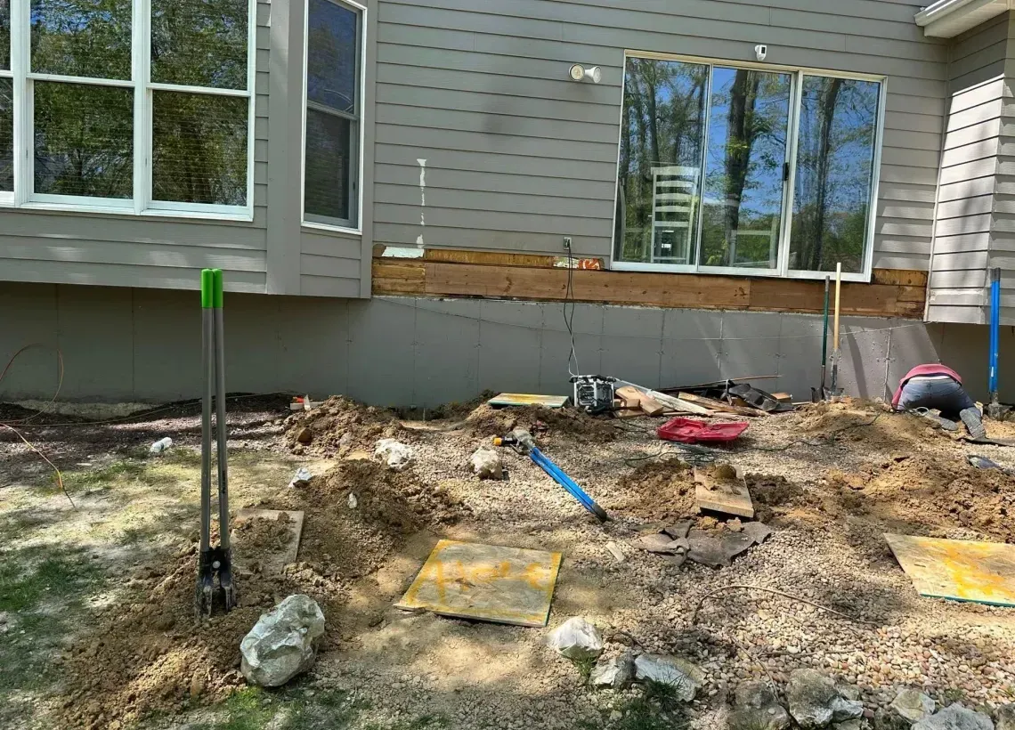 Backyard under construction with dirt, tools, and a house exterior in the background