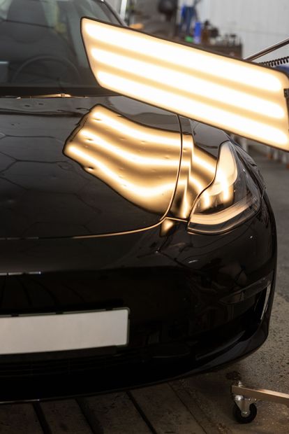 Black car front bumper with bright overhead light reflections in a garage