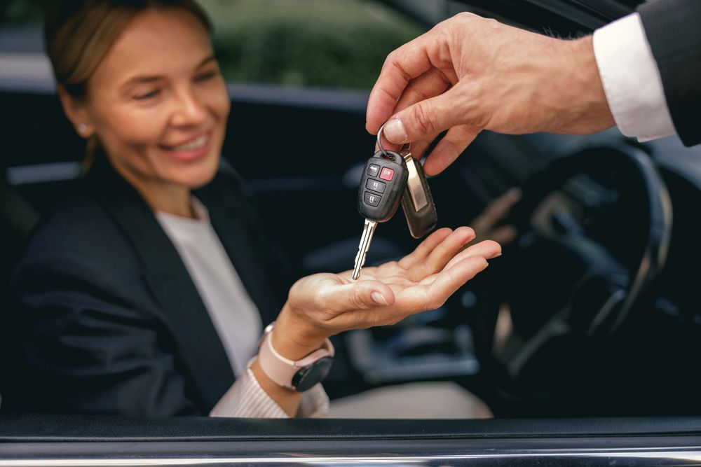 Consegna delle chiavi dell'auto a una persona sorridente seduta in un veicolo; primo piano di una chiave che viene passata.