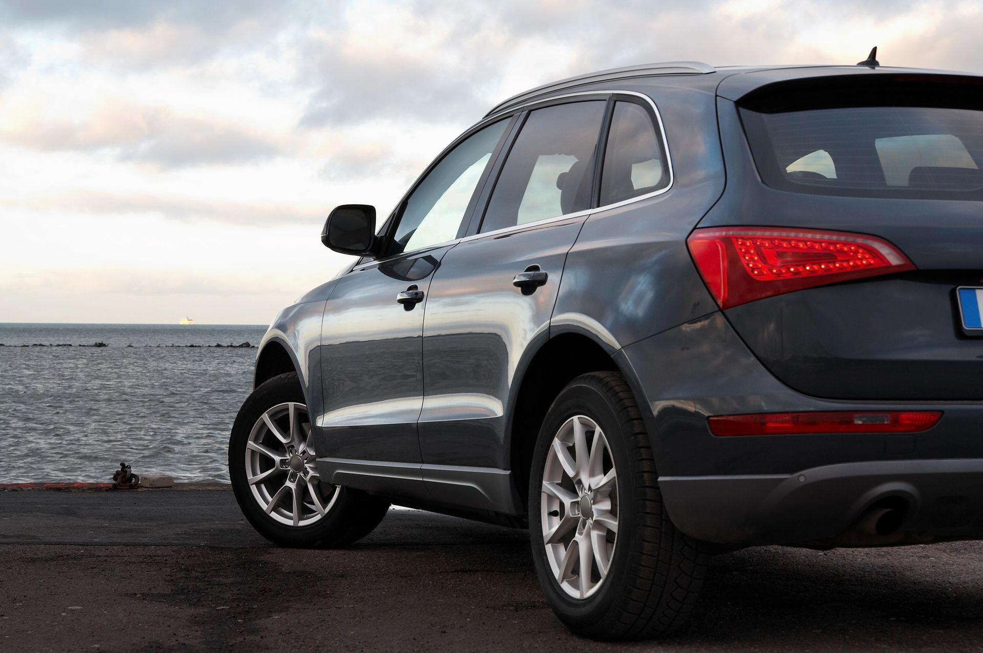 Un SUV grigio scuro parcheggiato vicino a uno specchio d'acqua con un cielo nuvoloso.