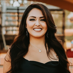 A woman in a black dress and necklace is smiling for the camera.