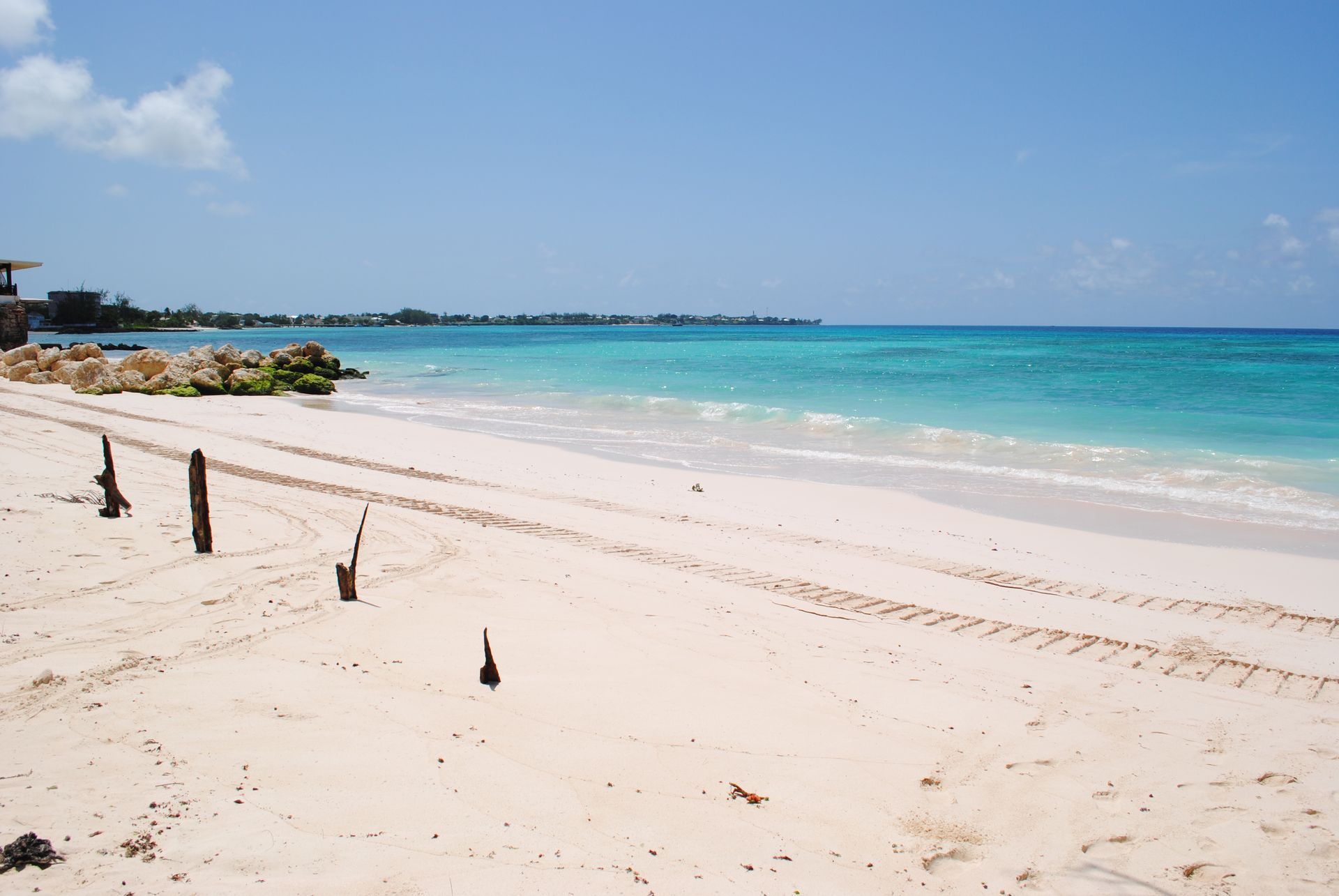 Sunny tropical beach with turquoise water, white sand, and a rocky shoreline under a clear sky