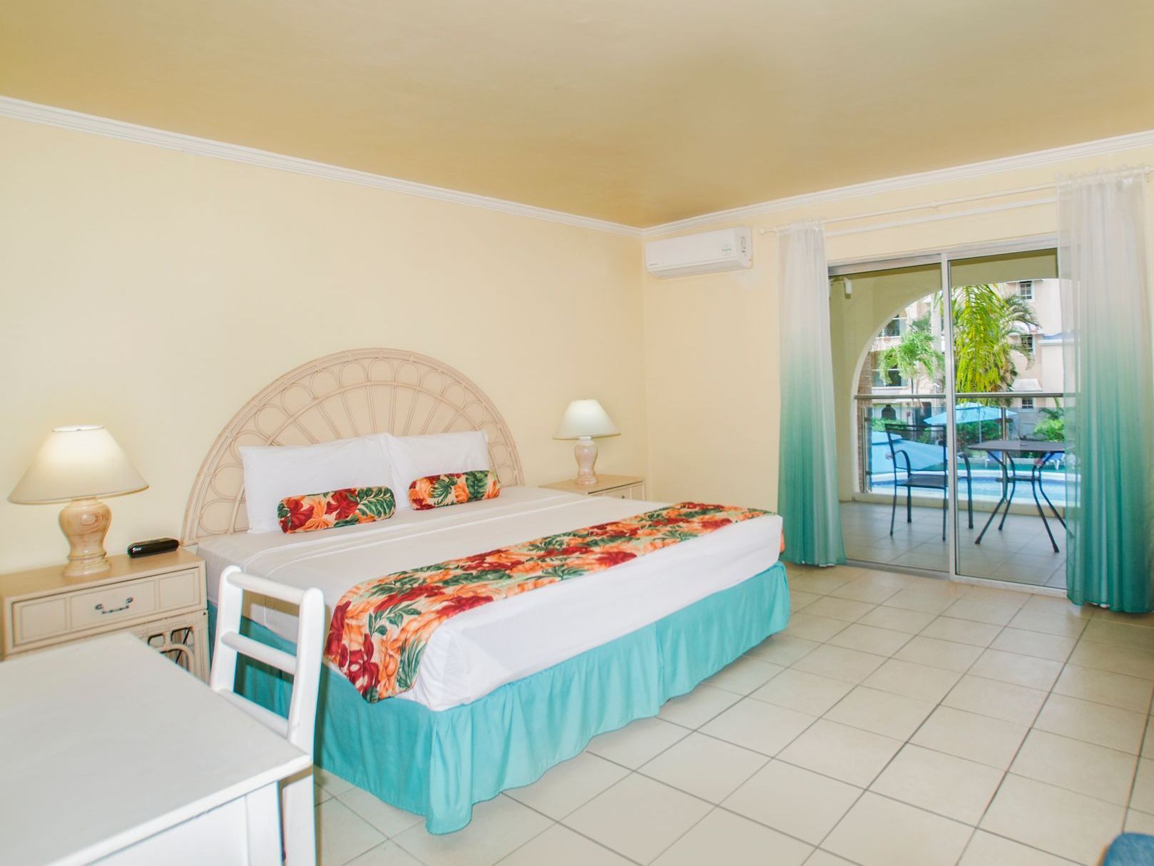 Bright bedroom with a bed, bedside lamps, tiled floor, and sliding glass doors to a patio.