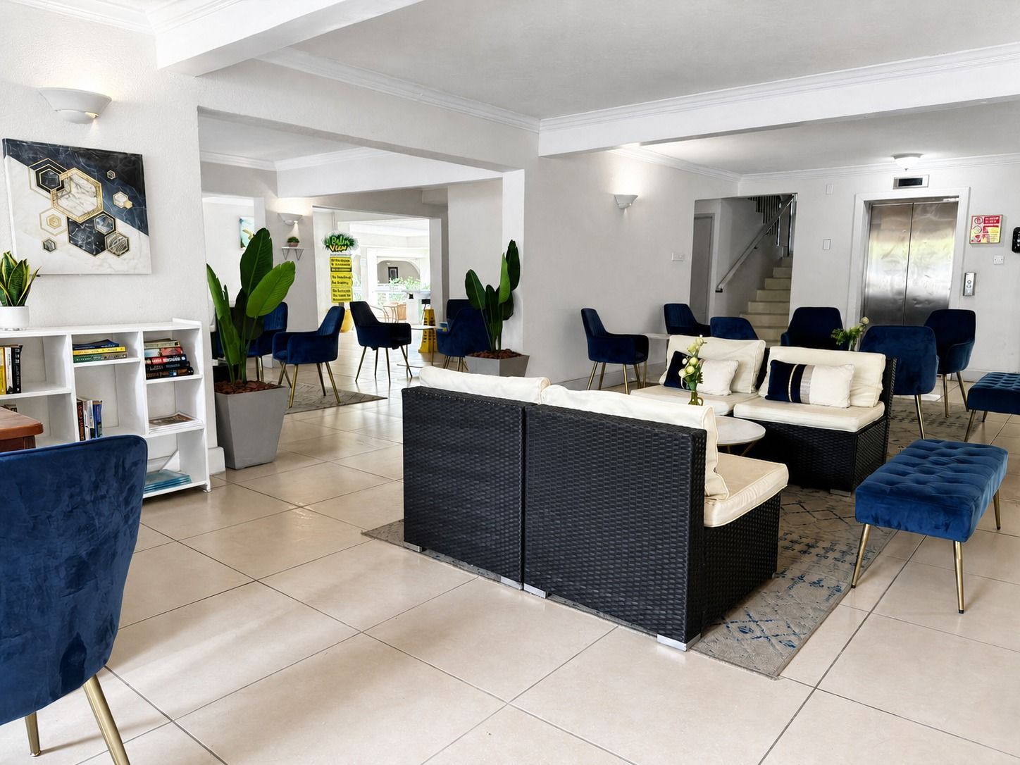 Bright modern lounge with white tile floors, blue chairs, plants, and a central cream sofa set