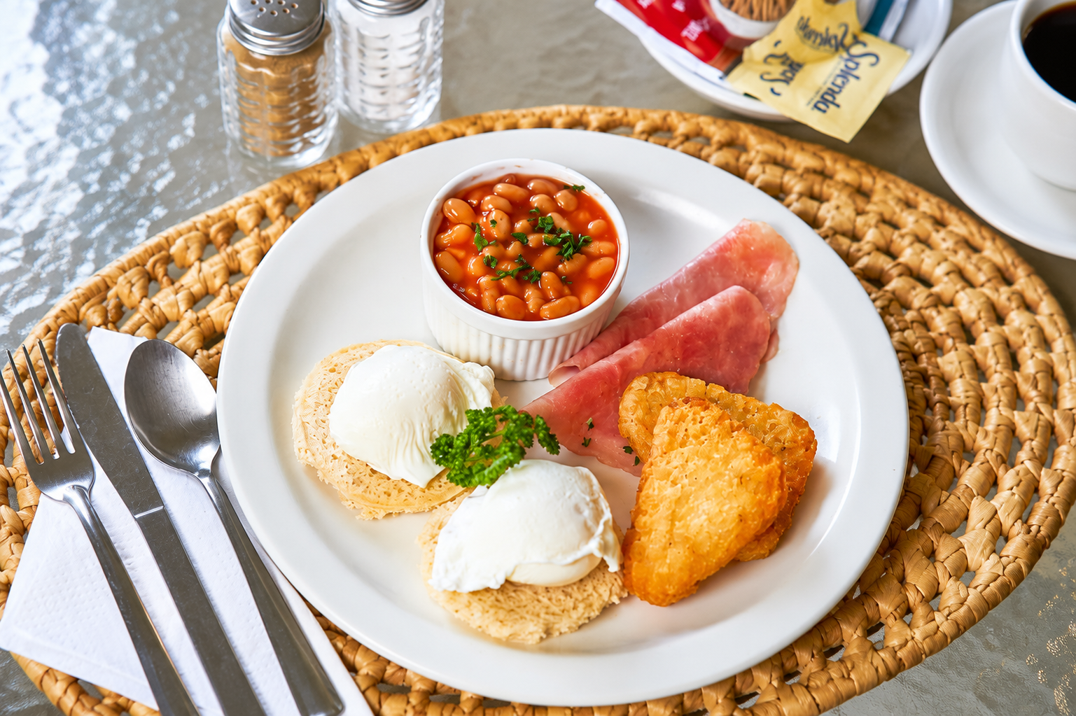 Breakfast plate with eggs, sausage, beans, toast, and hash brown on a woven placemat