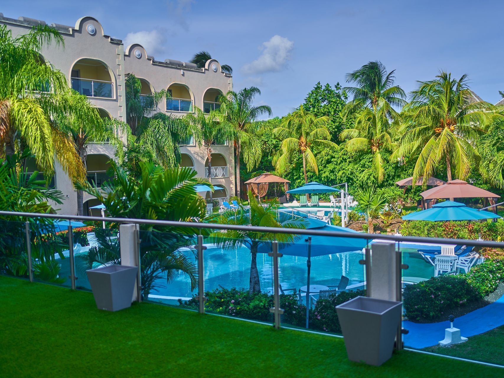 Resort pool and palm trees beside a white hotel building under a bright blue sky