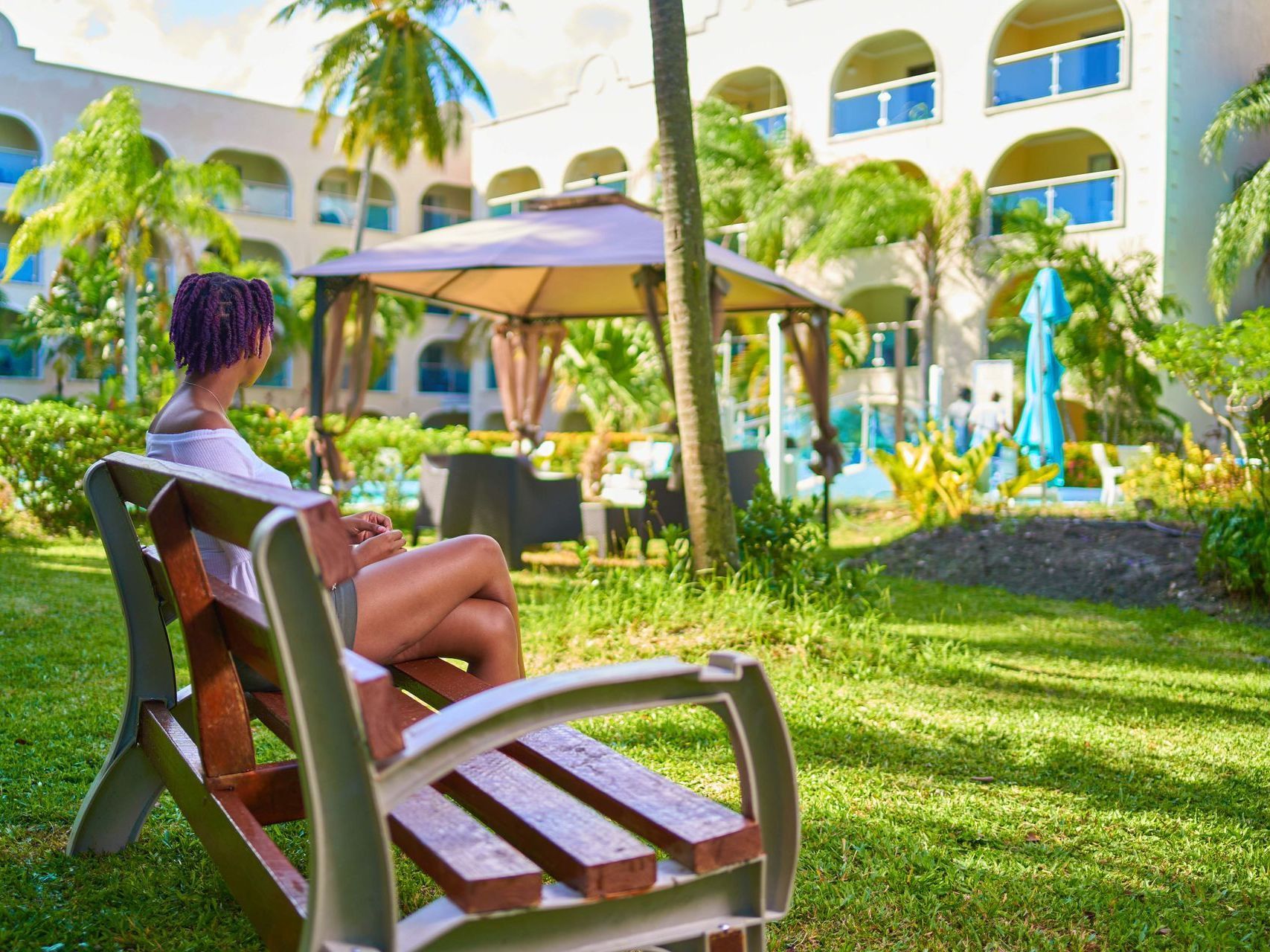 Person relaxing on a chair in a sunny tropical hotel courtyard with palm trees and a pool