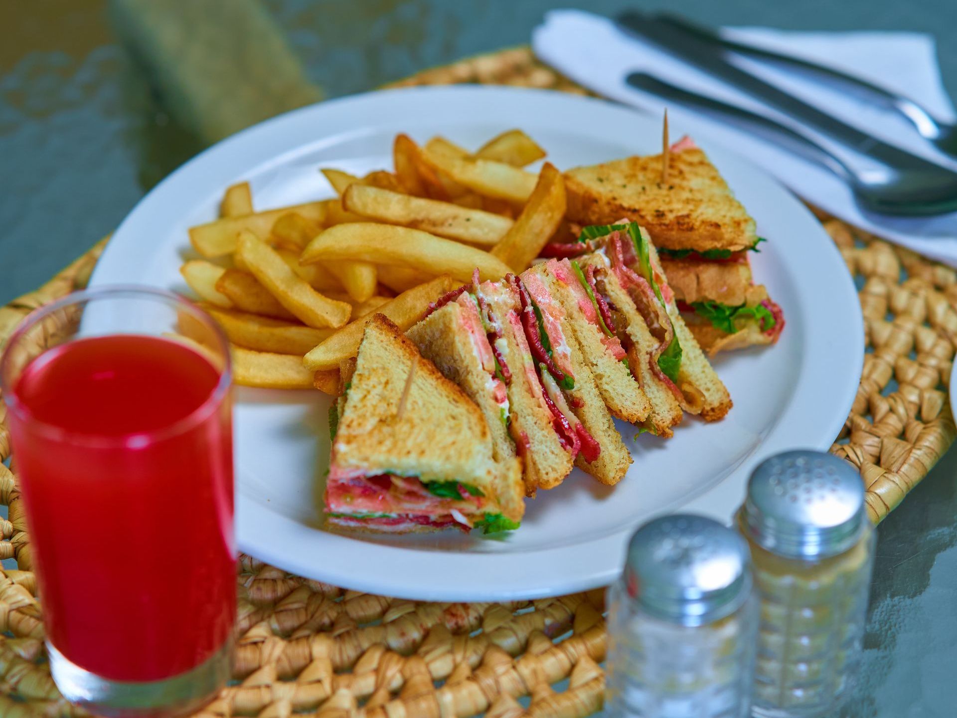 Club sandwich, fries, and a red drink on a white plate at a table