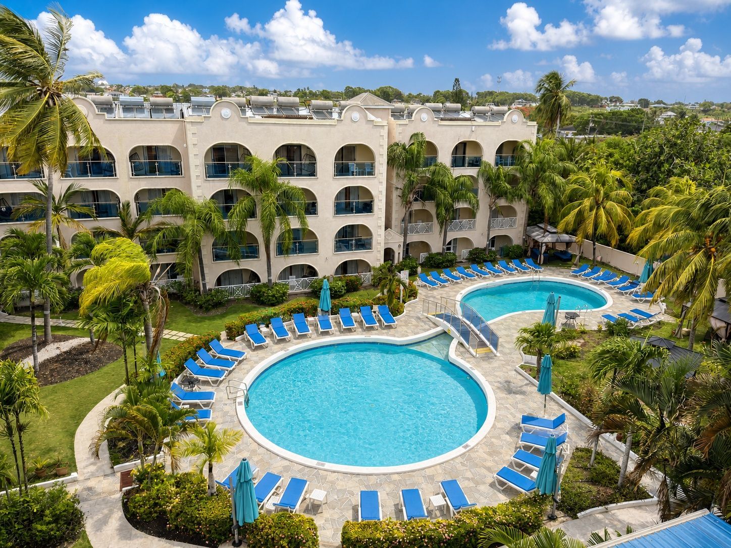 Resort courtyard with a large blue pool, loungers, palm trees, and a white arched hotel building