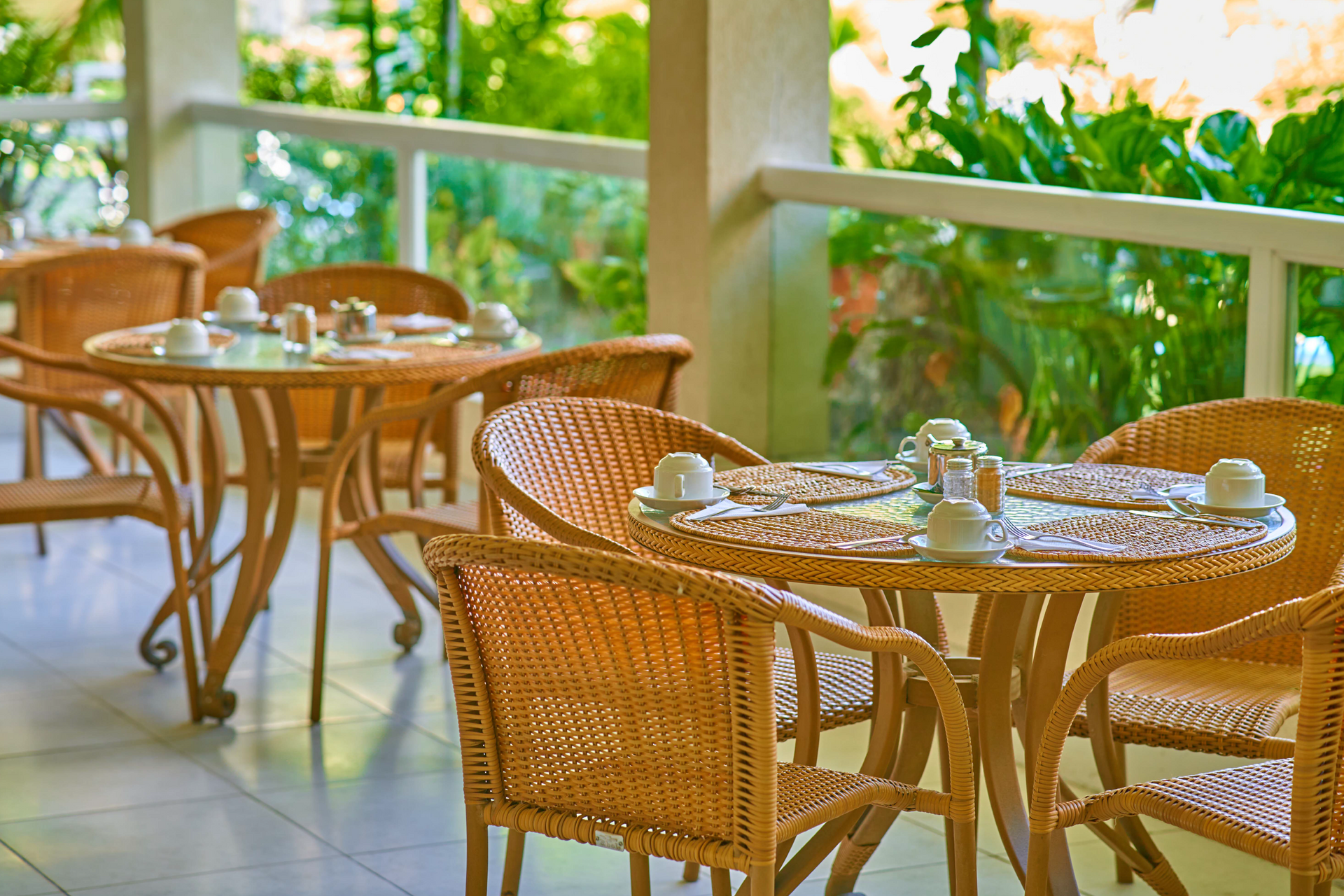 Wicker tables and chairs on a sunlit outdoor café patio with glasses and plates