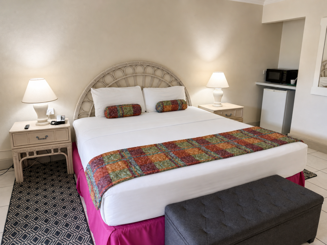Neatly made bedroom with a king bed, patterned bench, bedside lamps, and patterned rug