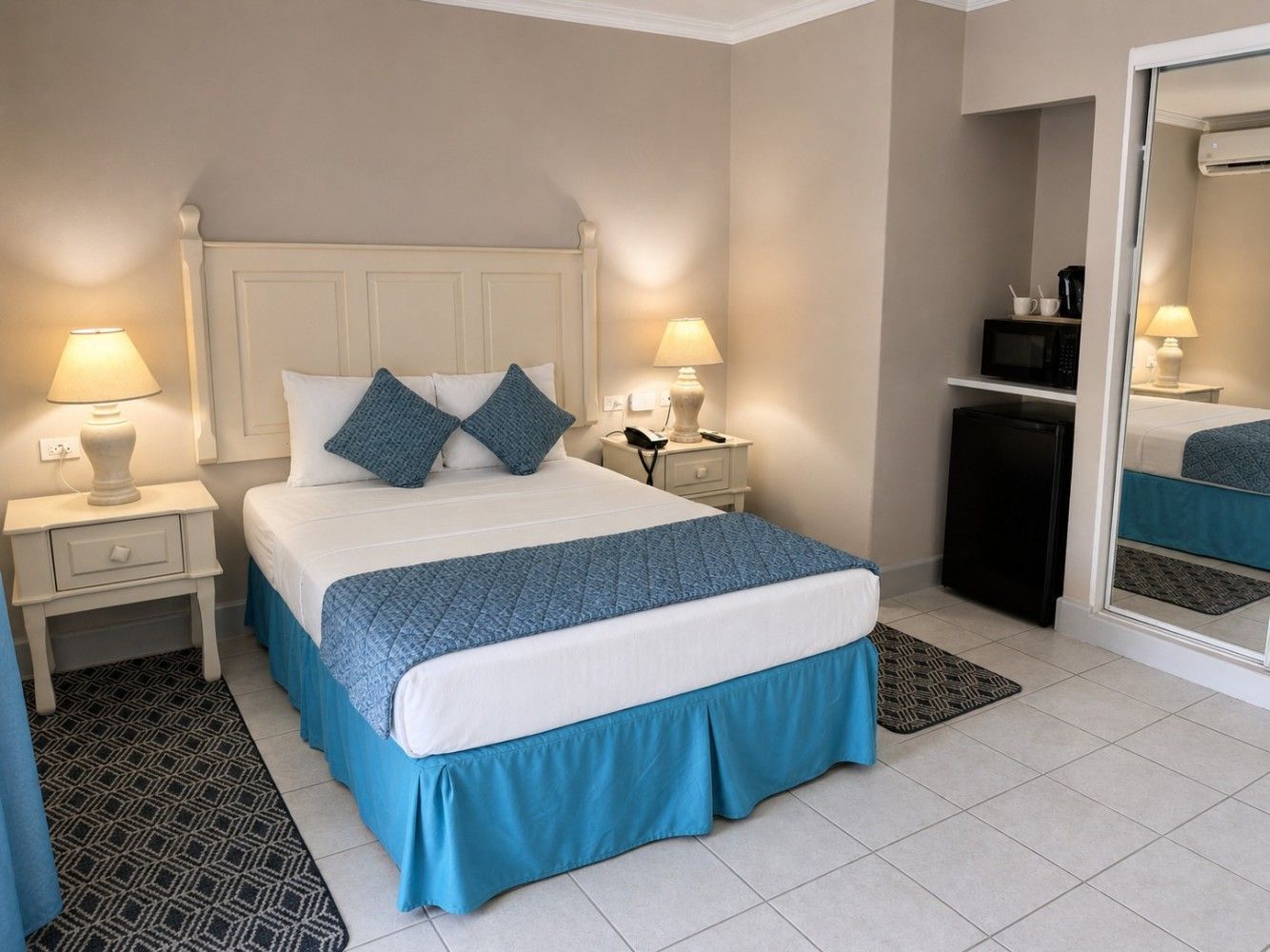 Neatly made bedroom with a white bed, blue accents, matching lamps, and mirrored closet doors