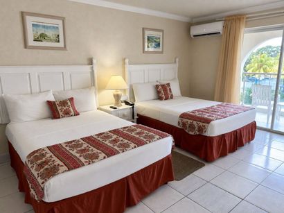 Bright twin bedroom with white beds, red accents, tiled floor, and a balcony view.