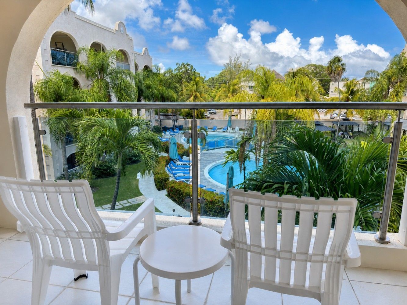 Balcony view of a tropical resort pool with white chairs and lush greenery