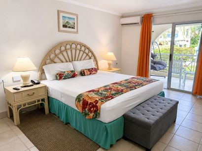 Bright bedroom with a white bed, orange curtains, wicker headboard, and balcony doors opening outside
