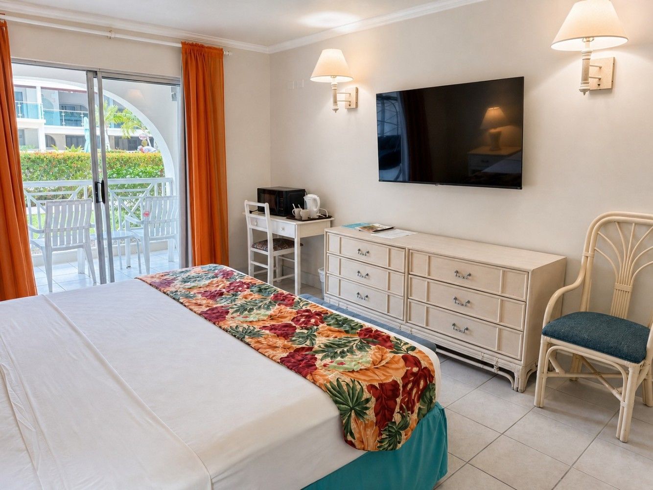 Bright bedroom with bed, wall-mounted TV, dresser, chair, and sliding glass doors to a patio