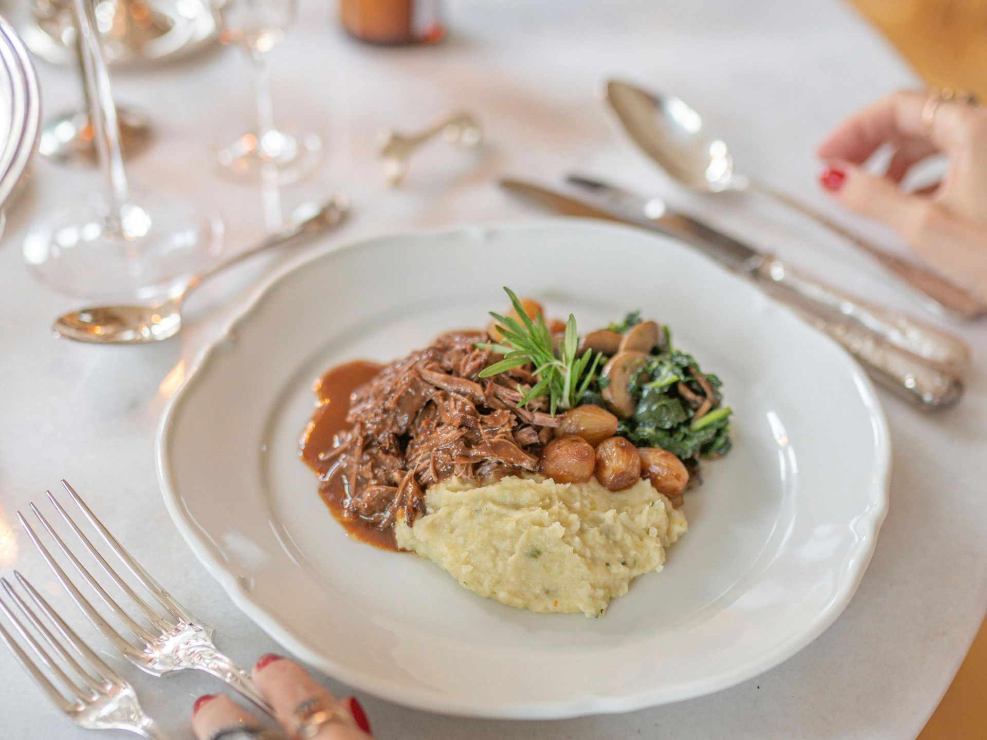 Plated gourmet meal with meat, mashed potatoes, and greens on a formal dining table