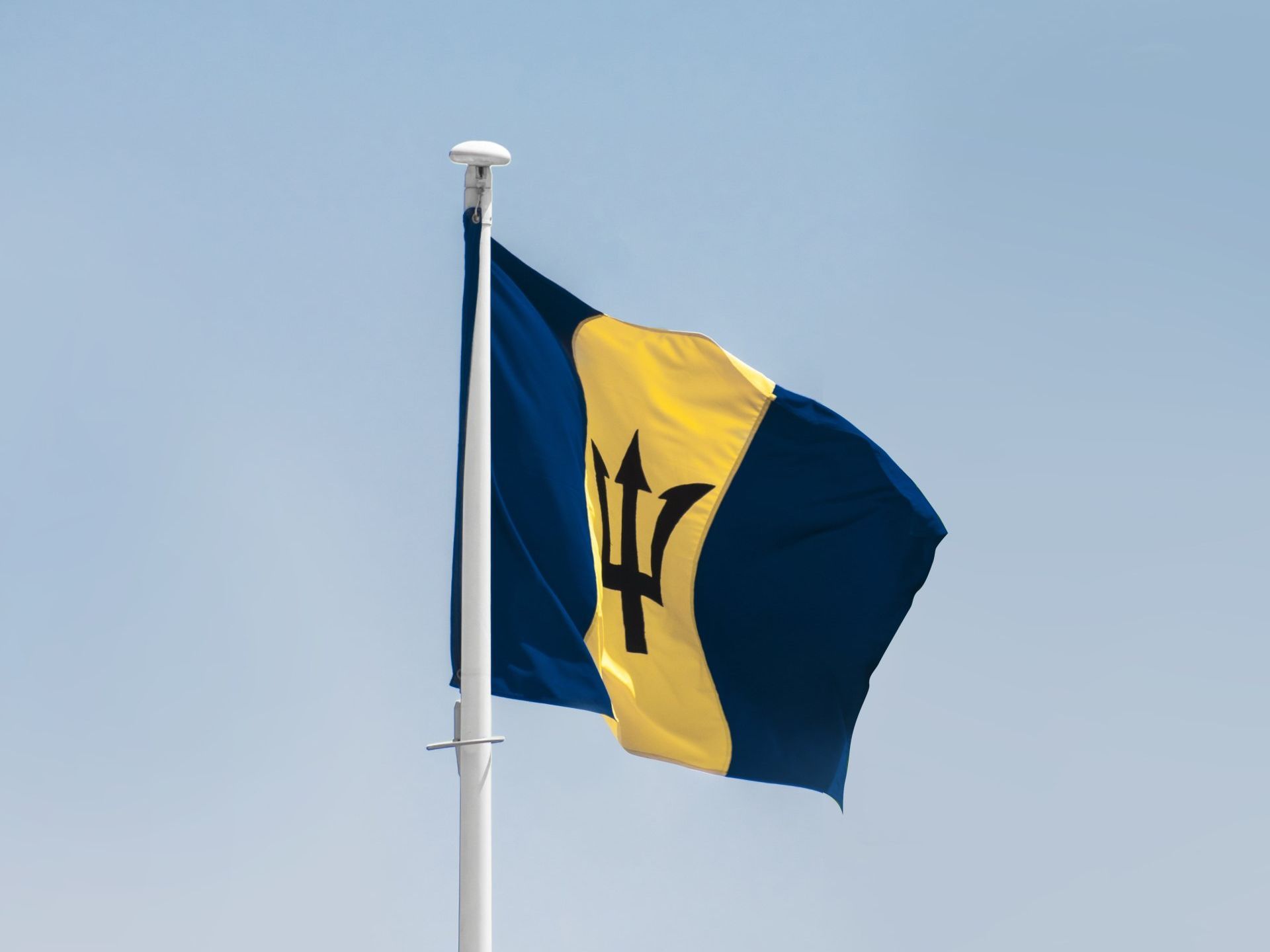 Barbados flag waving on a white flagpole against a clear blue sky