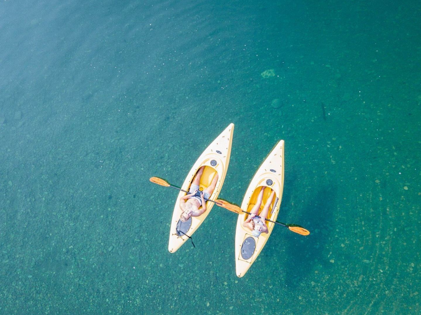 Two kayaks floating side by side on clear blue water, viewed from above