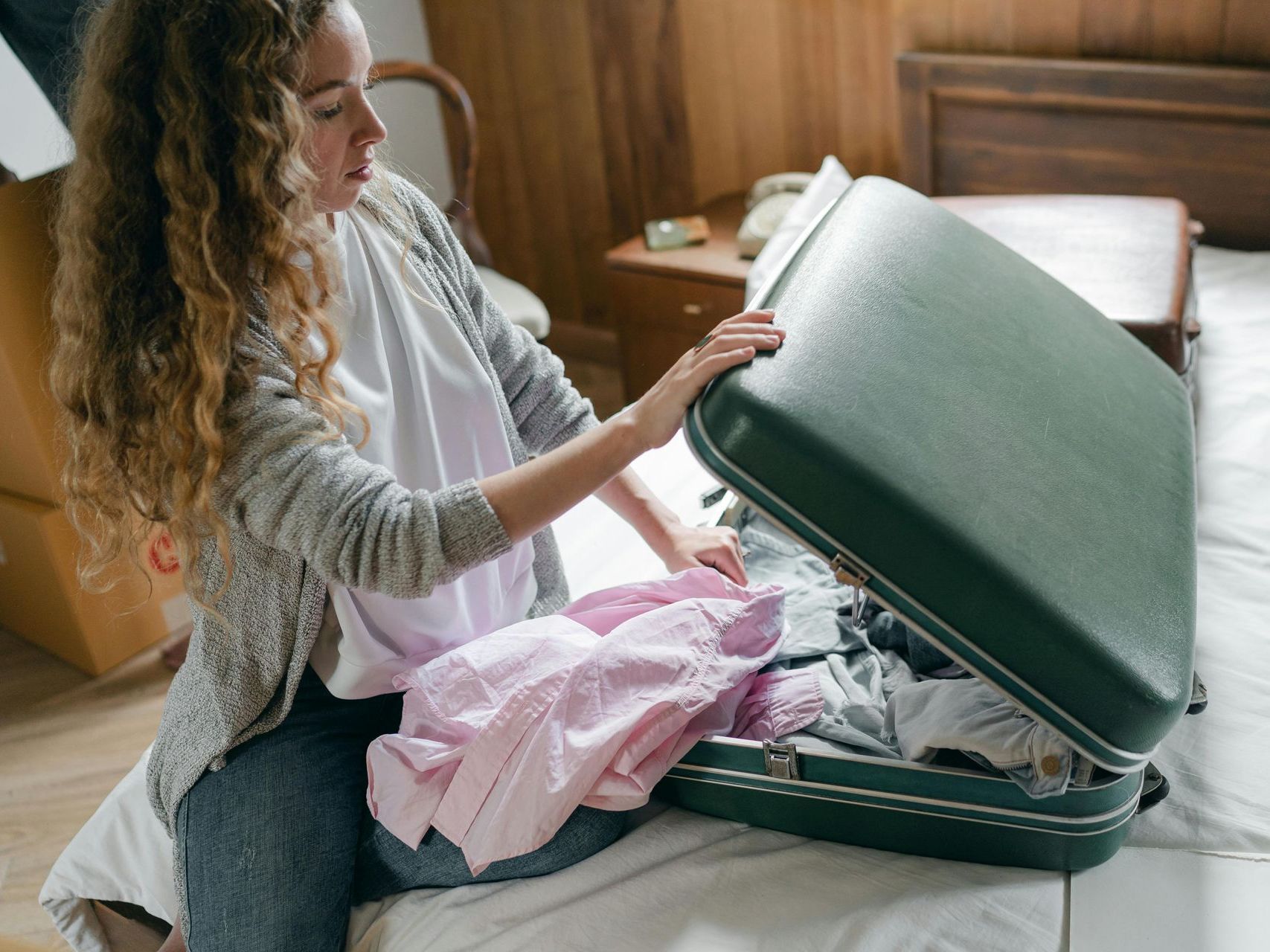 Woman packing clothes into an open suitcase on a bed by a window