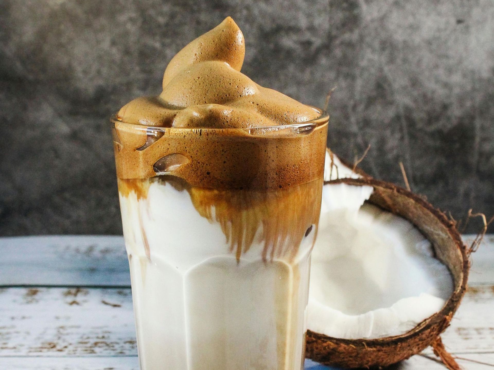 Iced dalgona coffee in a glass with coconut halves on a rustic wooden surface