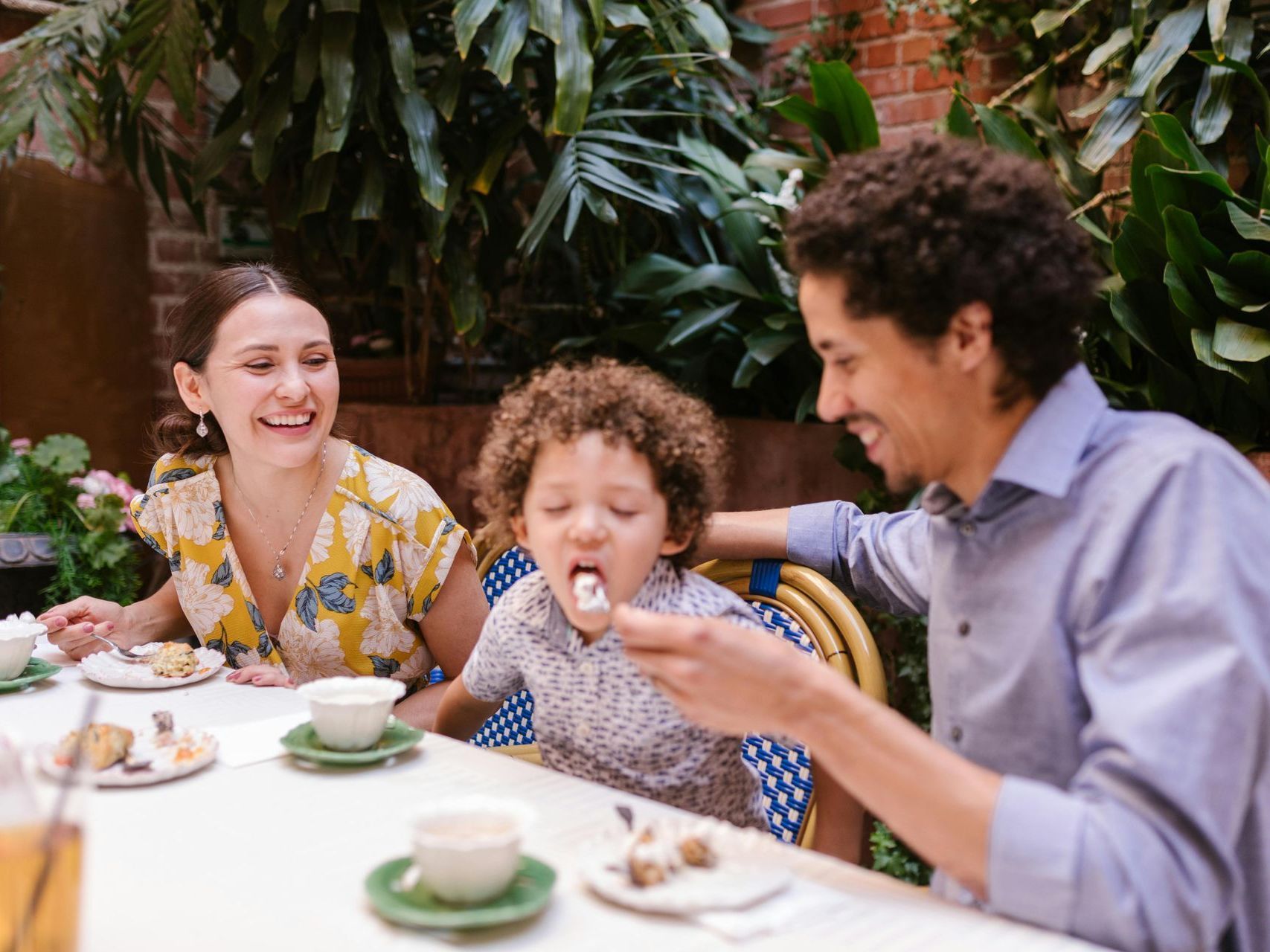 Family enjoying tea and snacks at an outdoor garden table, smiling and laughing together