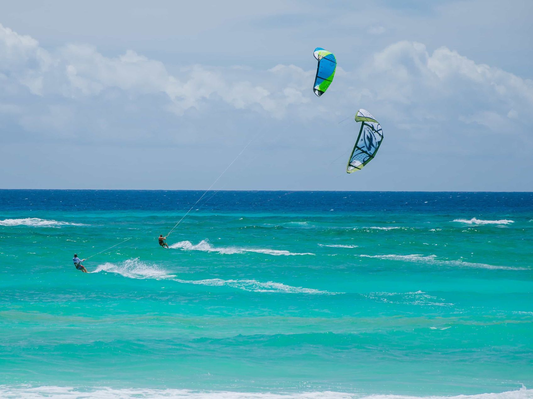Kitesurfers on turquoise ocean with two colorful kites under a cloudy sky
