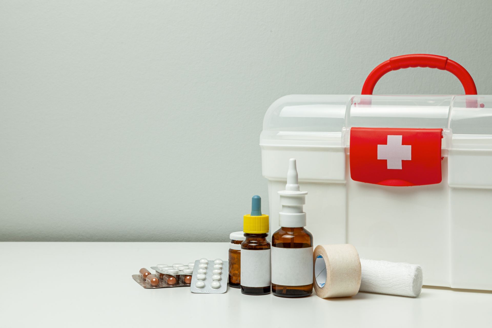 First-aid kit with red cross, medicine bottles, pills, and a bandage on a white surface