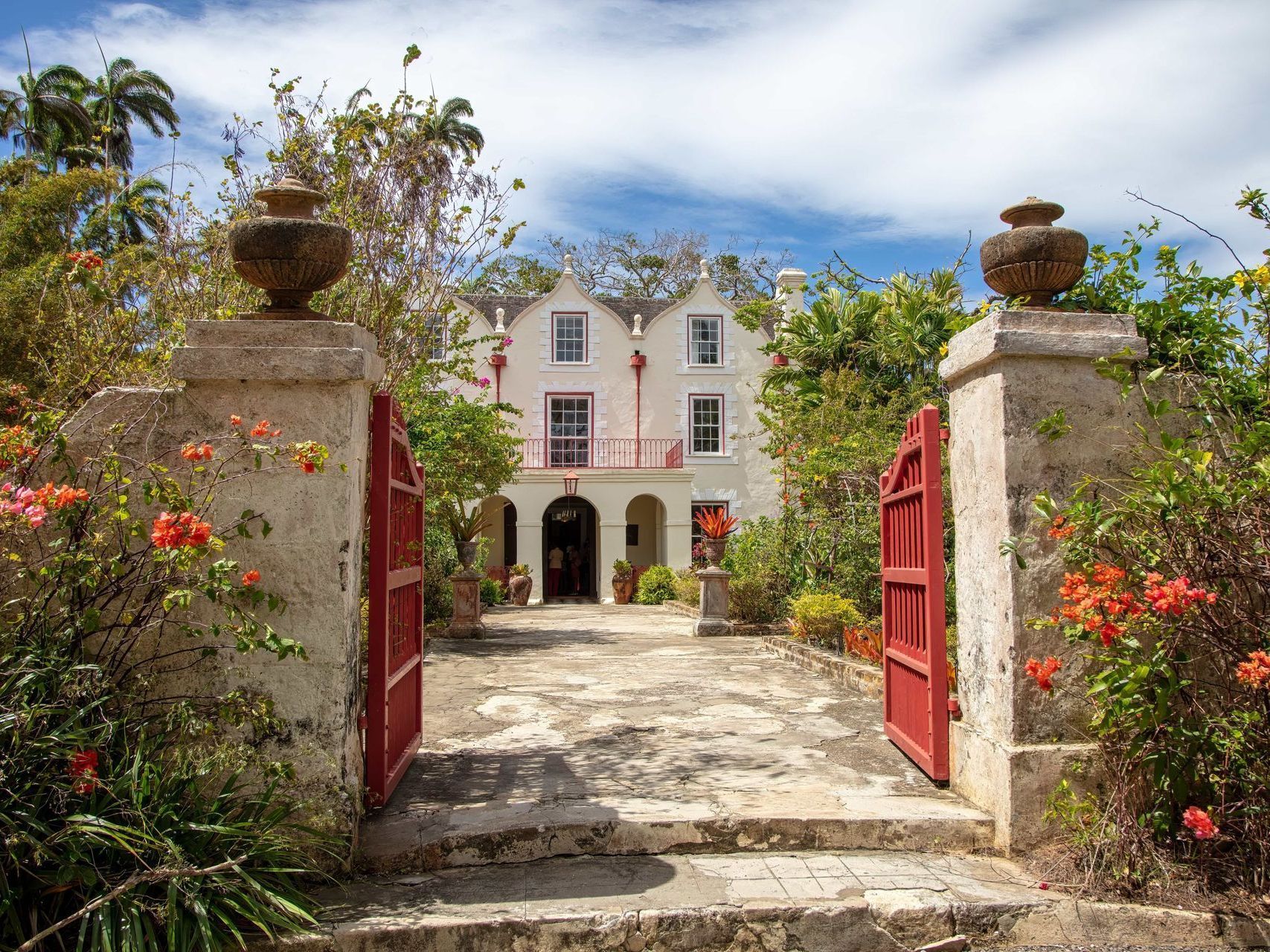 Stone gate with open red doors leading to a white house and garden path