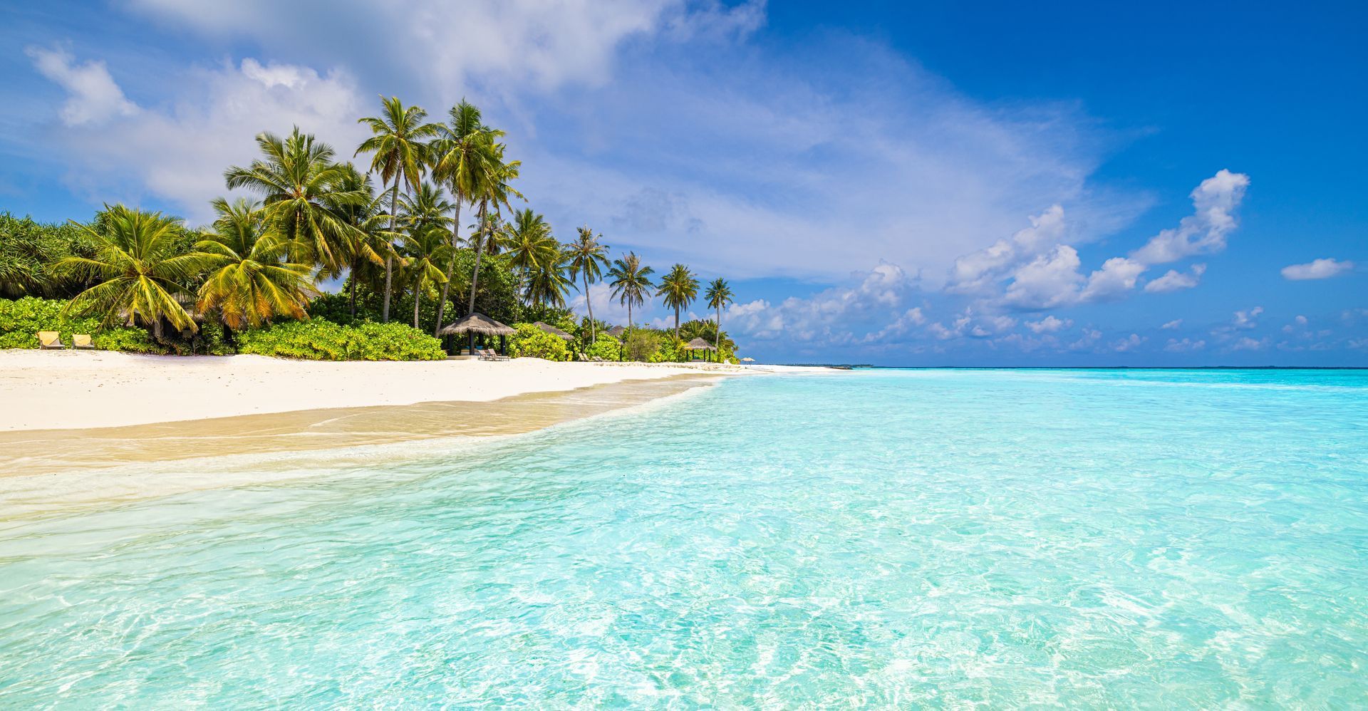 Tropical beach with white sand, palm trees, and clear turquoise water under a blue sky