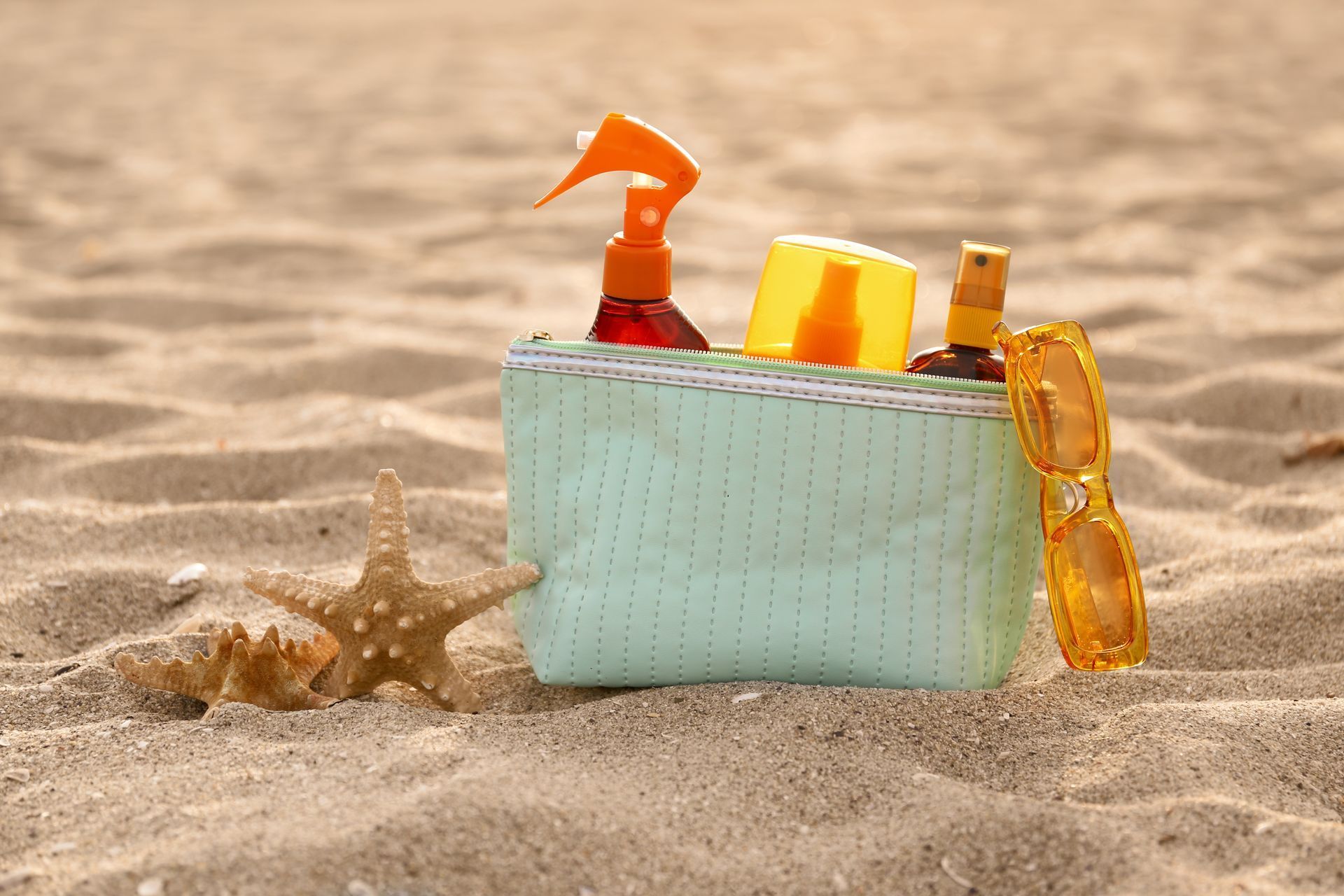 Beach tote with sunscreen, goggles, and towel beside a starfish on sand