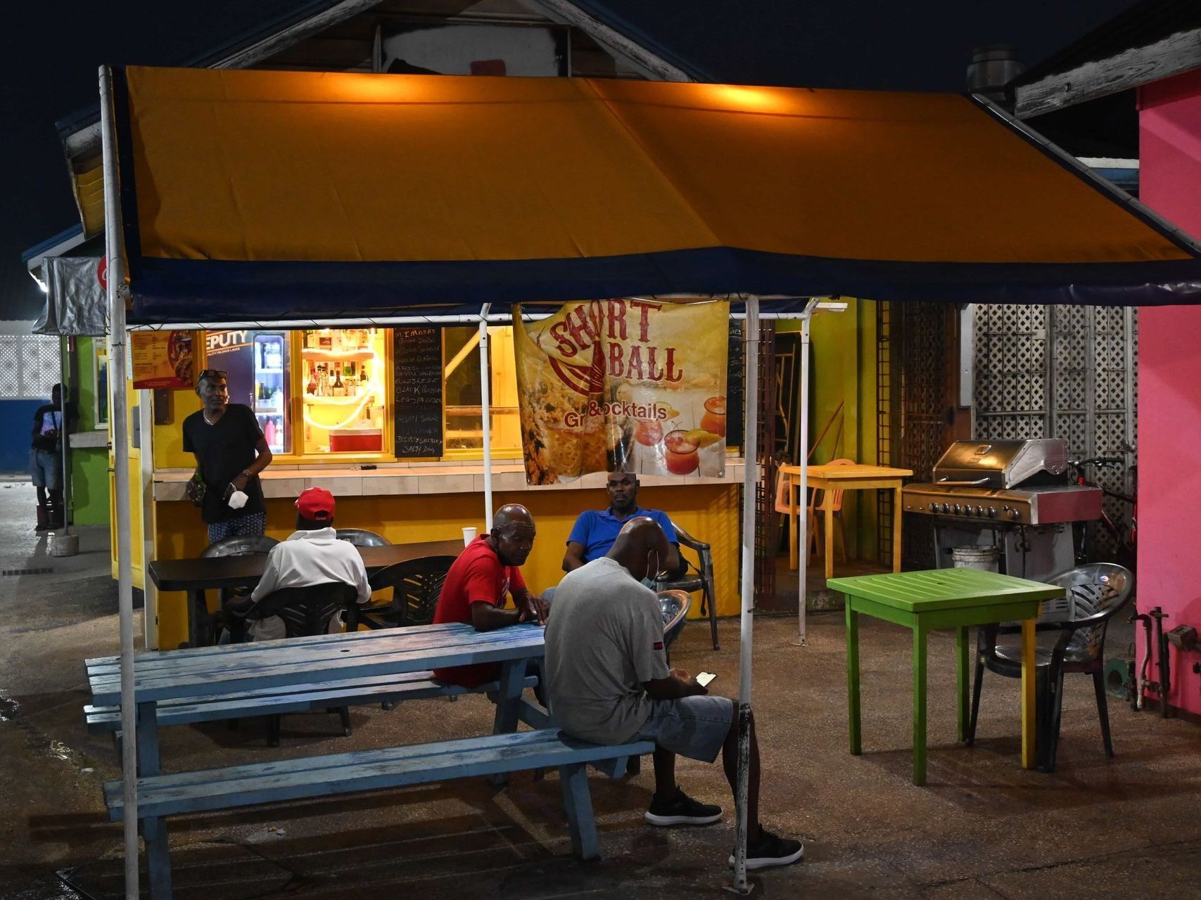 Outdoor food stall at night with seated customers under an orange awning and lit counter