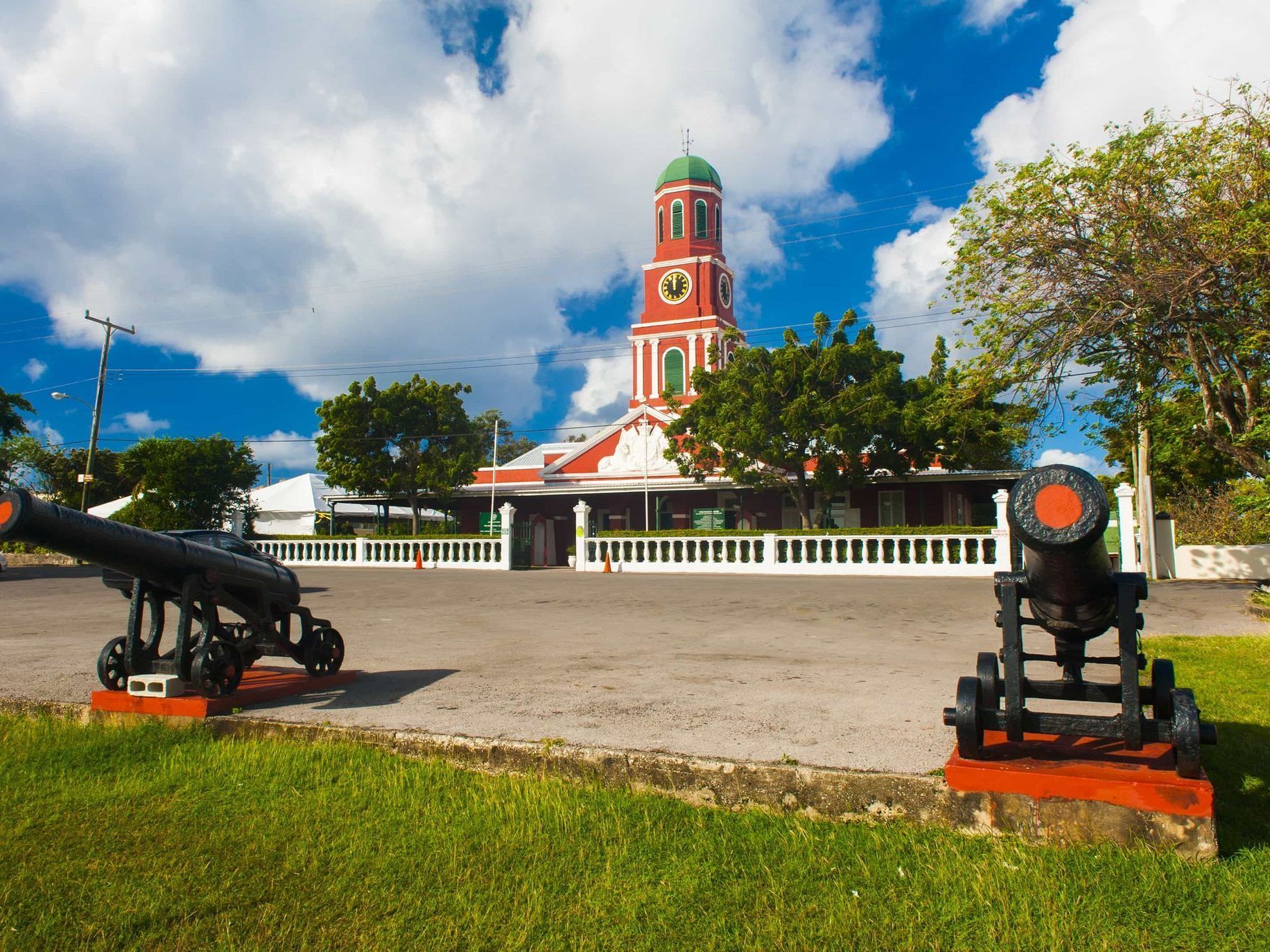 Historic red-and-white church tower behind cannons on a grassy plaza under a bright blue sky