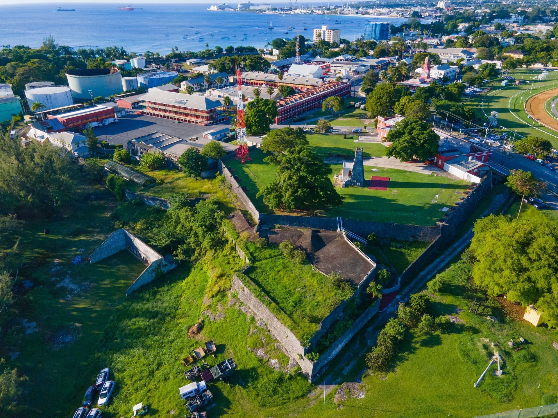 Aerial view of a coastal town with rooftops, green hills, roads, and the ocean in the distance