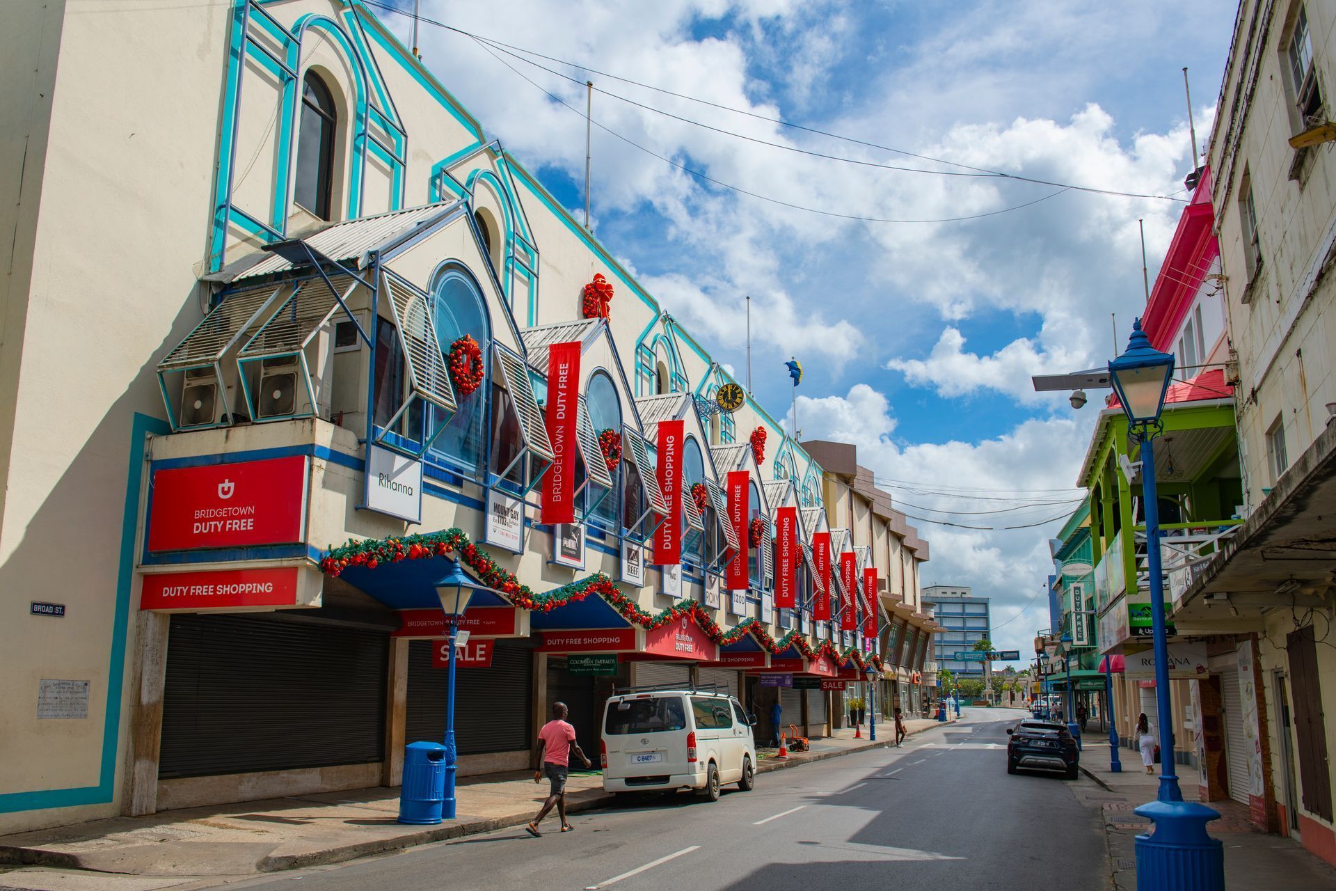 Colorful street with red-and-blue buildings, parked cars, and a partly cloudy sky