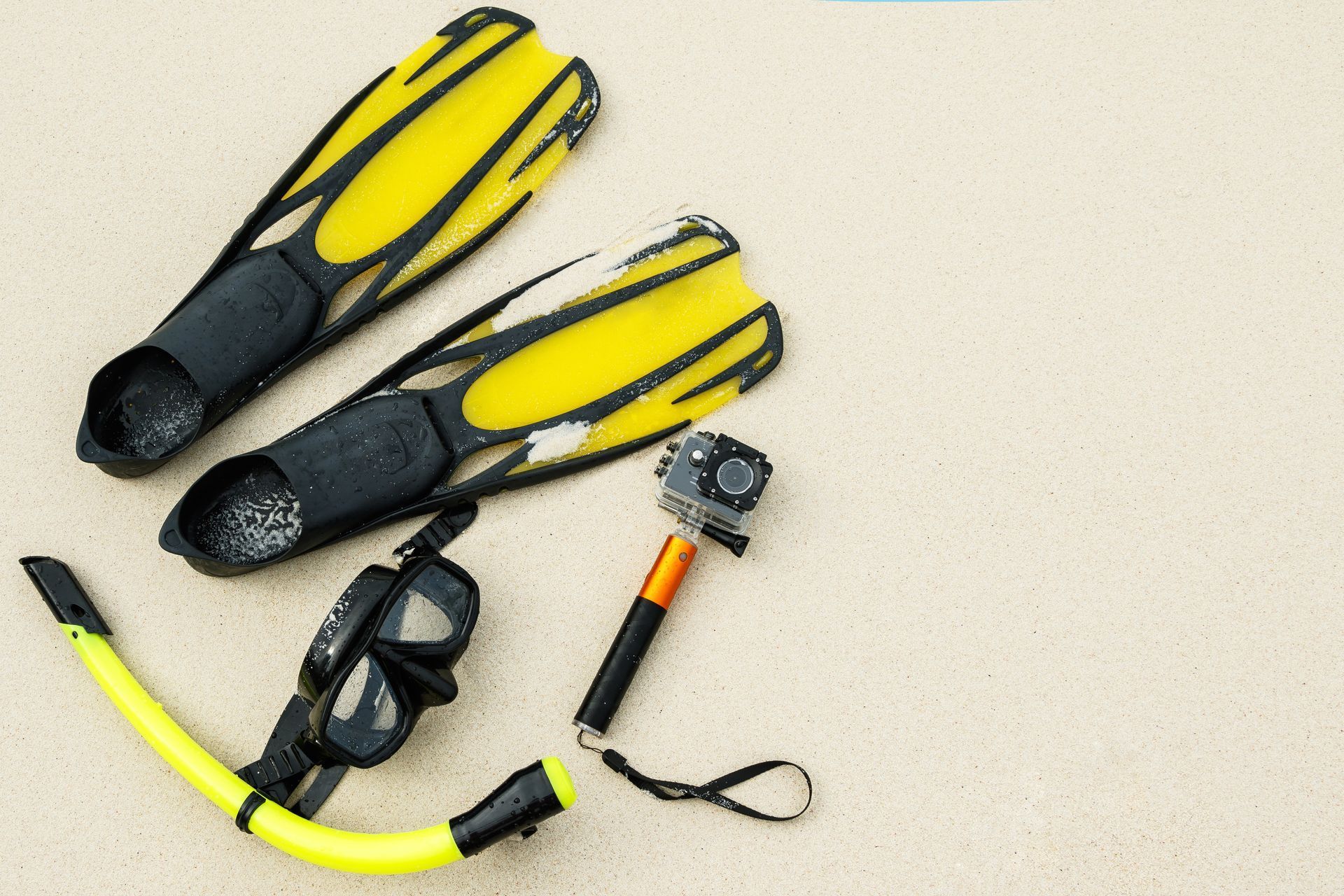 Yellow and black snorkeling fins, mask, snorkel, and camera accessory on a beige surface