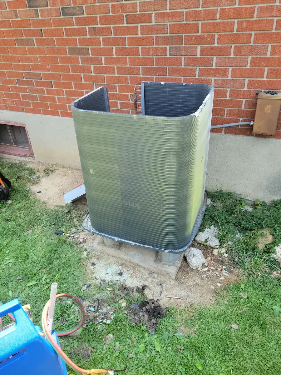 An air conditioner is sitting in the grass in front of a brick building.
