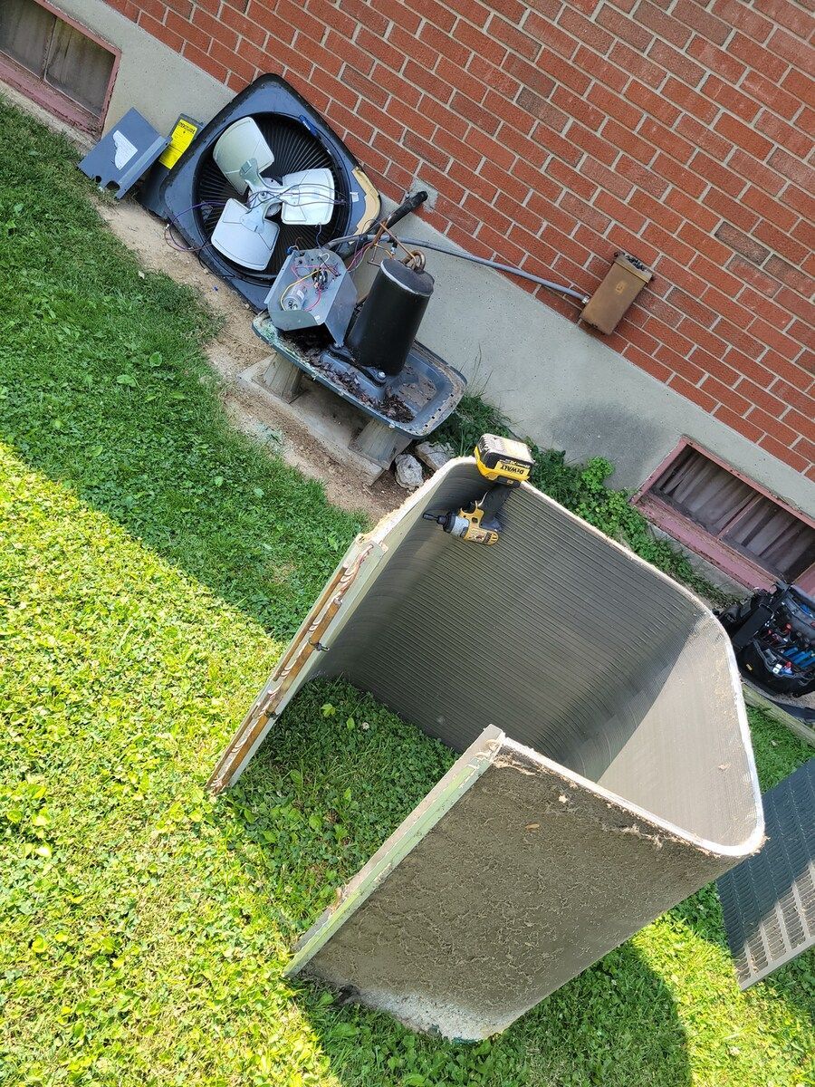 A broken air conditioner is sitting on the grass in front of a brick building.