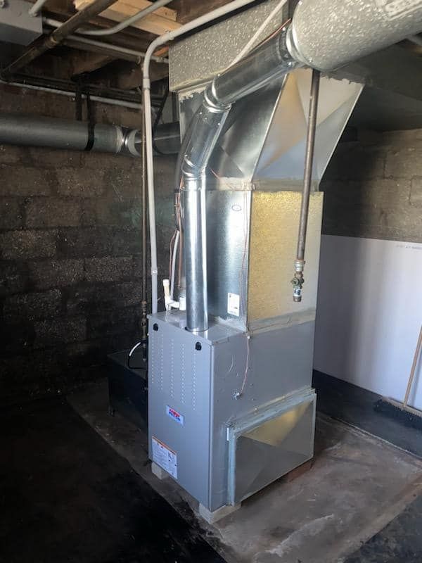 A large air conditioner is sitting in a basement next to a brick wall.