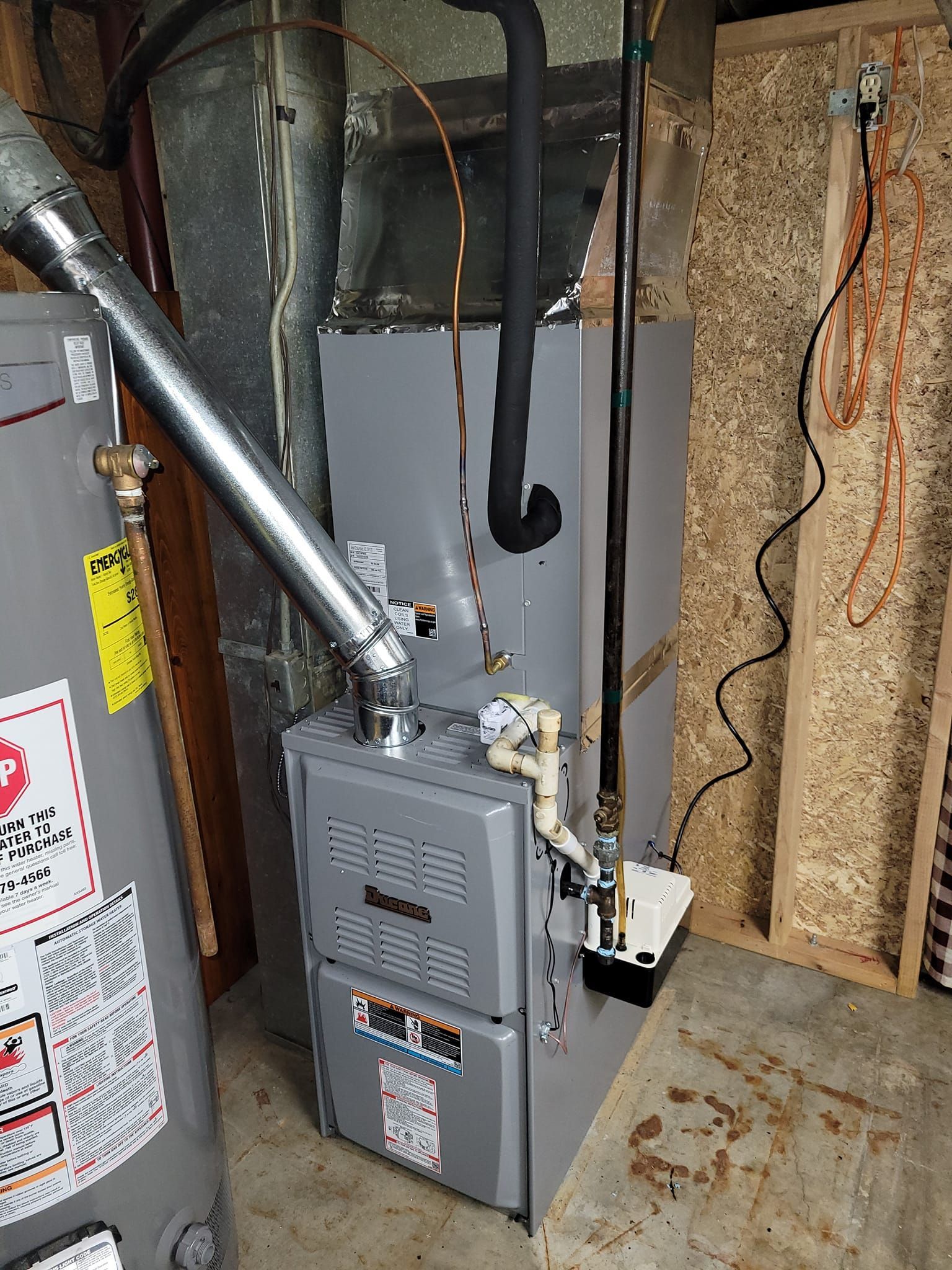 A gas heater is sitting in a basement next to a water heater.