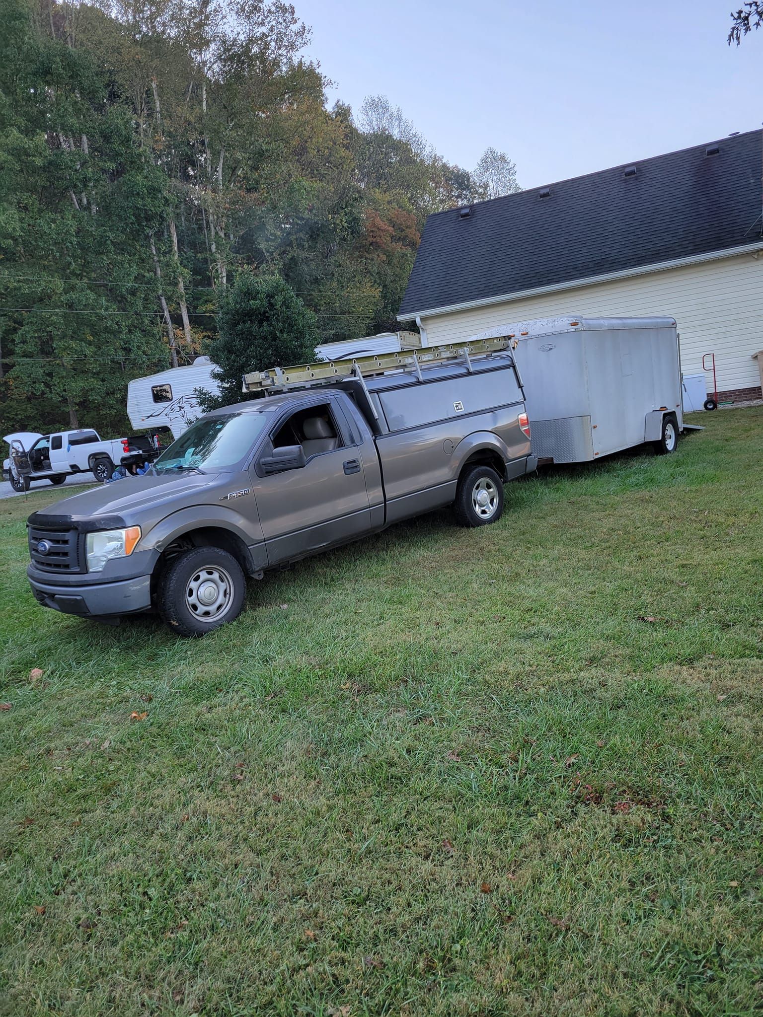 A truck with a trailer attached to it is parked in a grassy field.