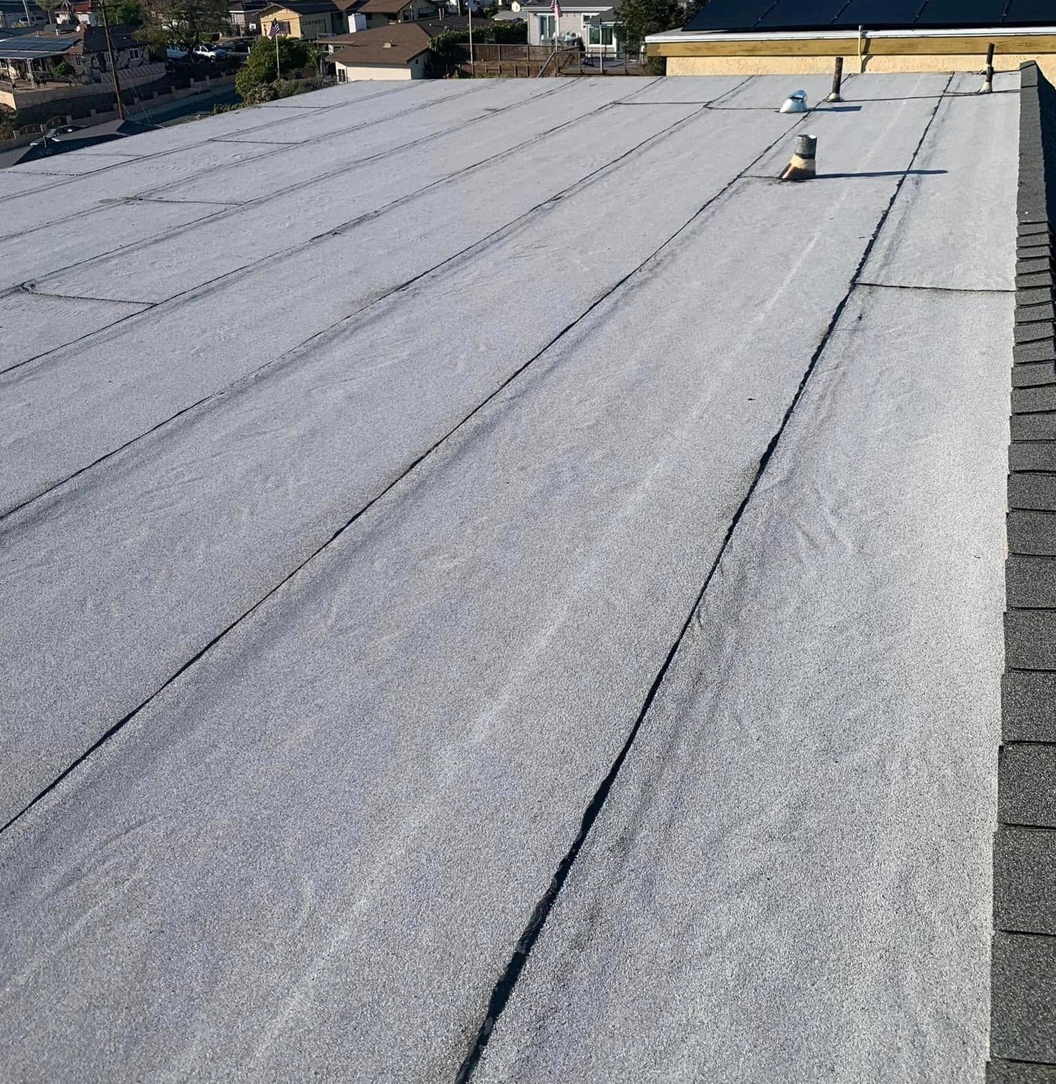 Flat gray rooftop with seams and two vent pipes under a clear sky