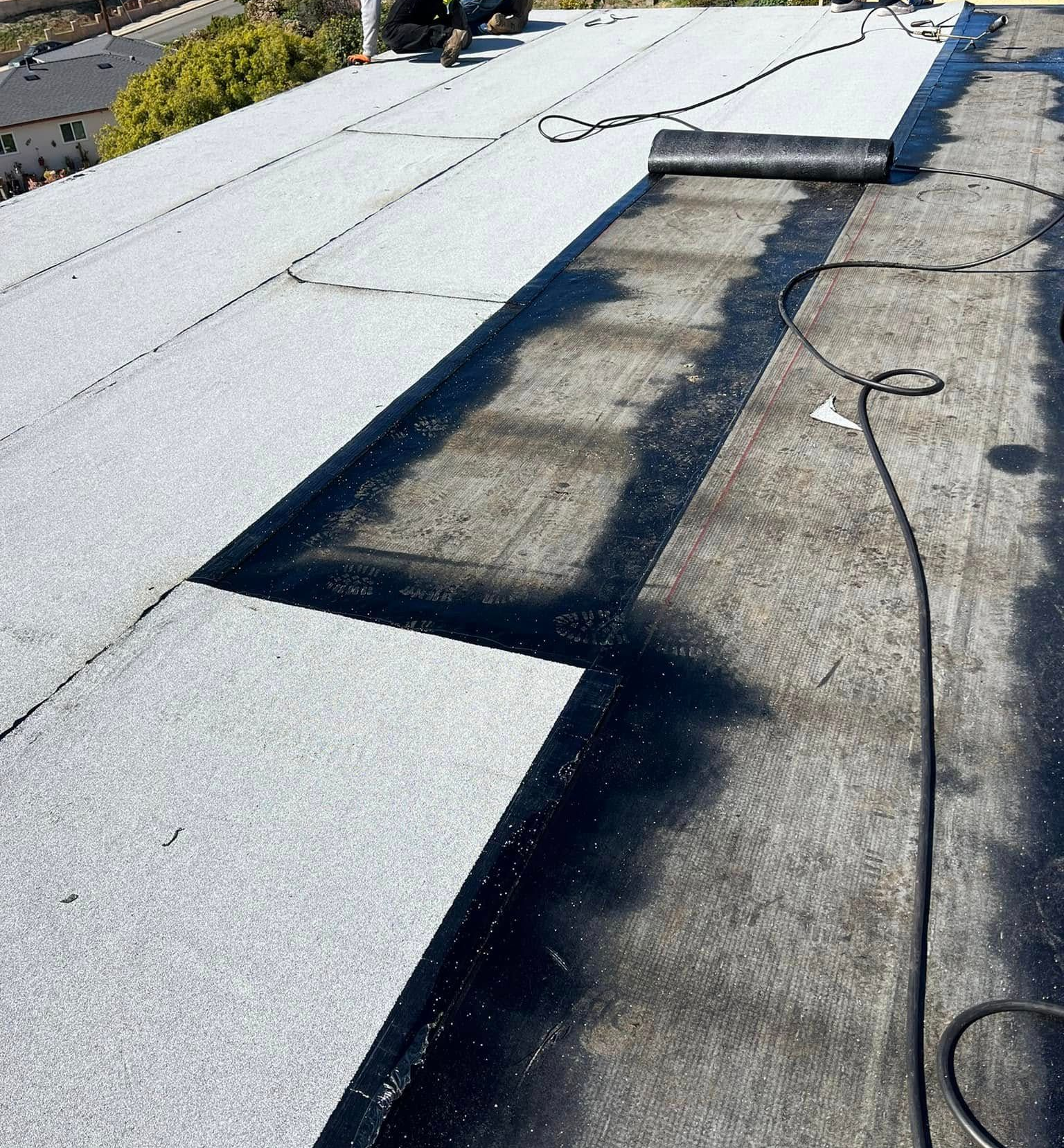 Roof work with white roofing panels partly installed over a dark roof section and a coiled cable.
