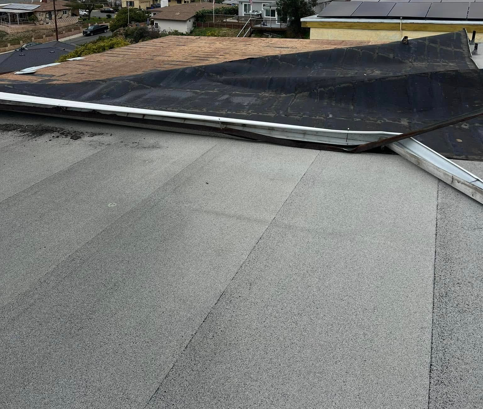 Roof with gray shingles meeting a black, flat section and a white edge trim, viewed from above