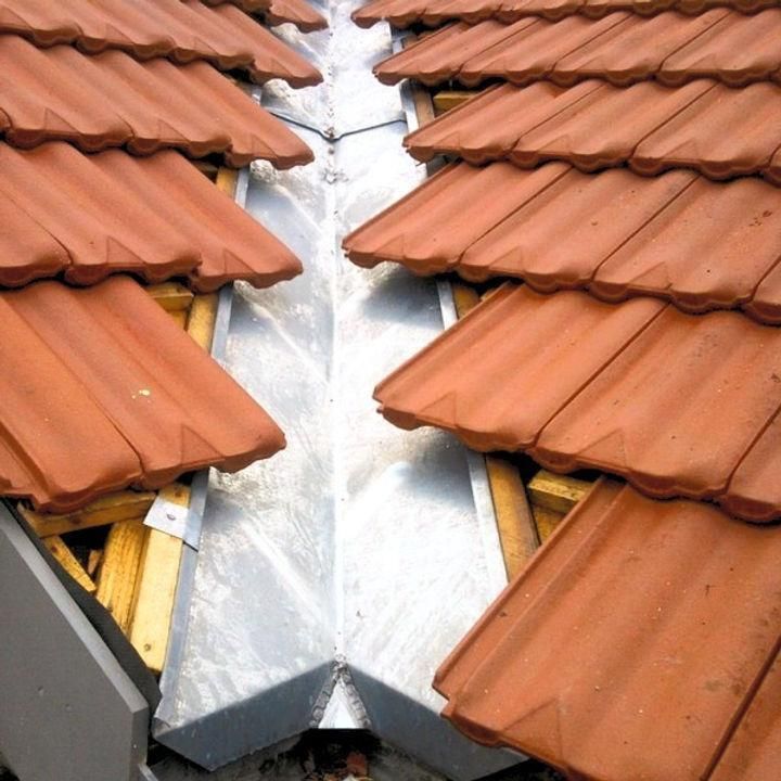 Red clay roof tiles around a silver metal gutter flashing in a roof valley