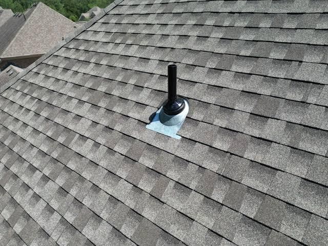 Brown shingled roof with a black vent pipe against a blue sky