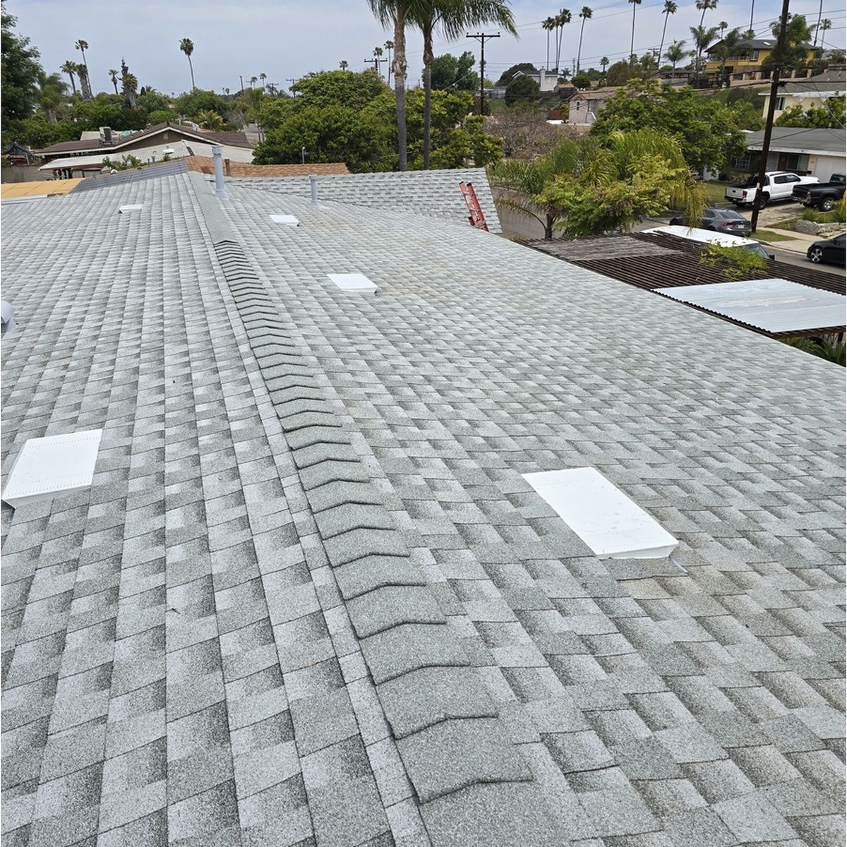 Gray shingle rooftop with white roof vents, overlooking a suburban neighborhood and palm trees